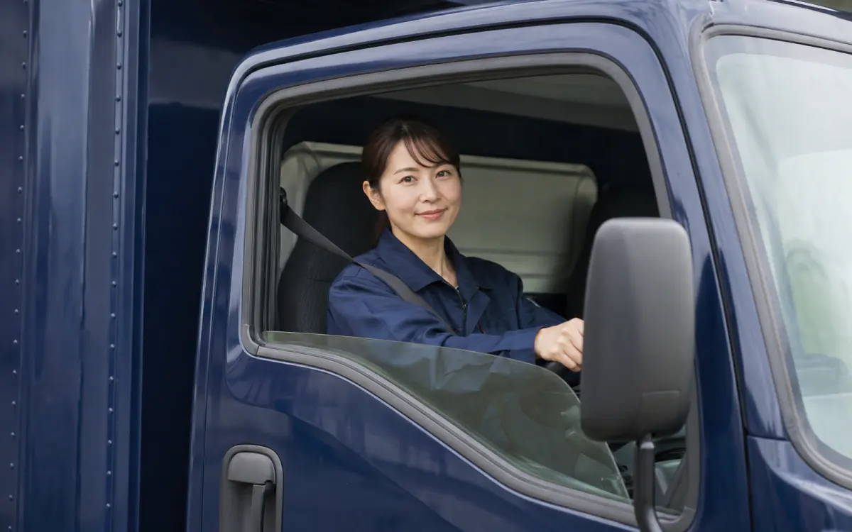 2tトラックの運転席で微笑む30代の女性ドライバー